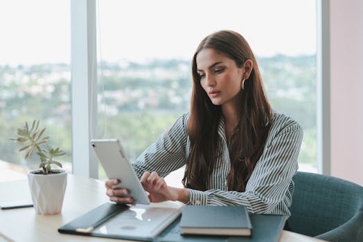 Confident businesswoman using a tablet while sitting at a desk in a modern office setting.